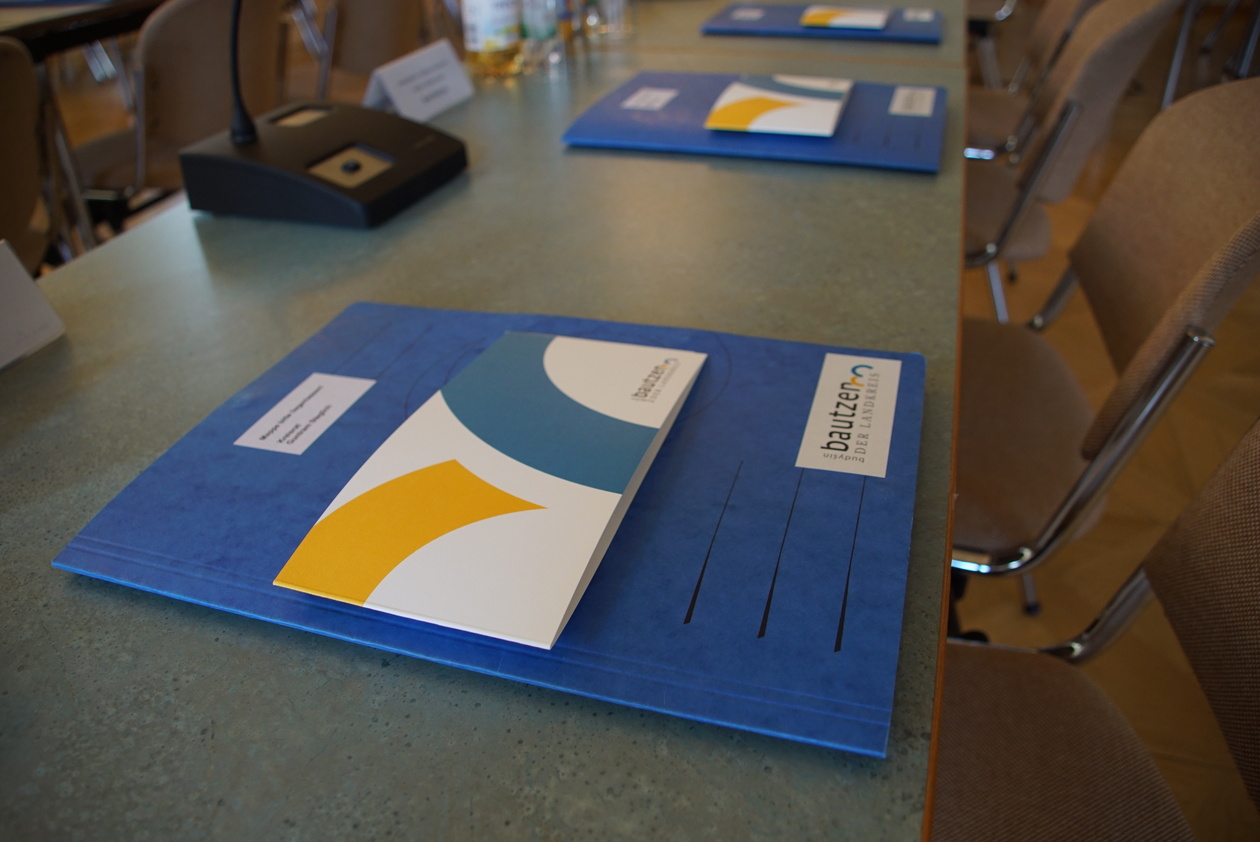 Das Foto zeigt eine blaue Mappe auf einer Tischoberfläche, darauf liegt eine Klappkarte im Design des Landkreises Bautzen.