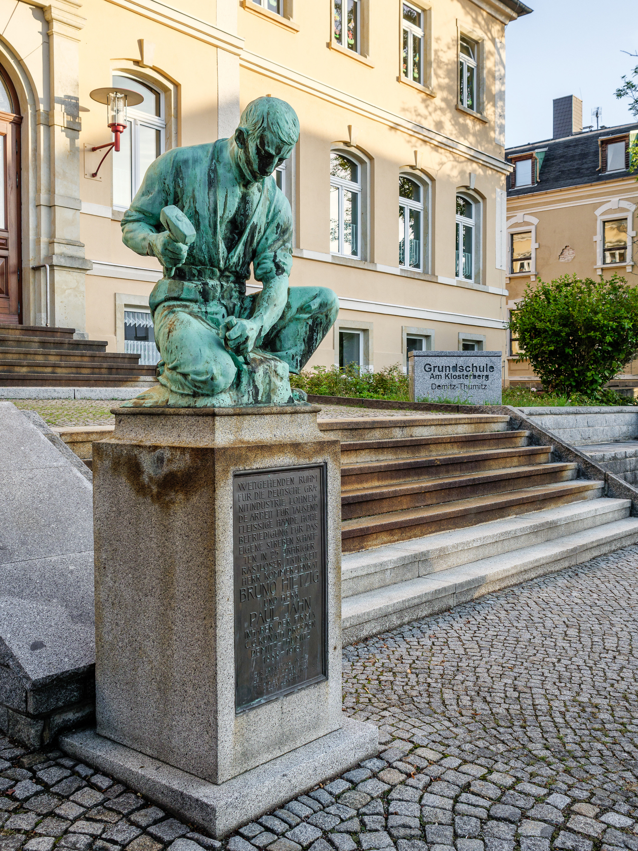 Das Bild zeigt das Denkmal eines Steinarbeiters vor einem Gebäude
