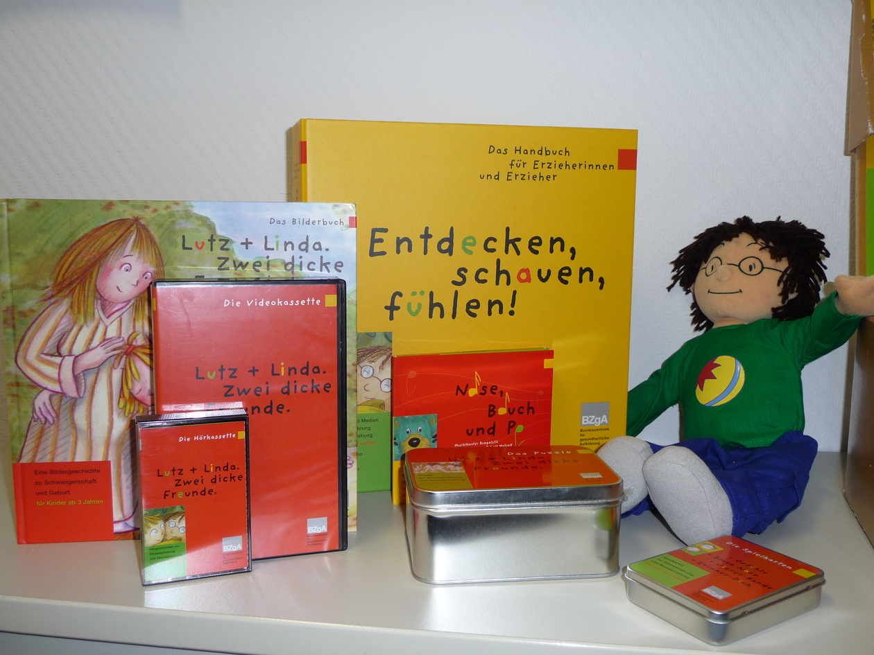 Das Bild zeigt den Inhalt der Kindergartenbox: verschiedene Medienträger, zwei Kinderbücher , eine Puppe und zwei Blechdosen