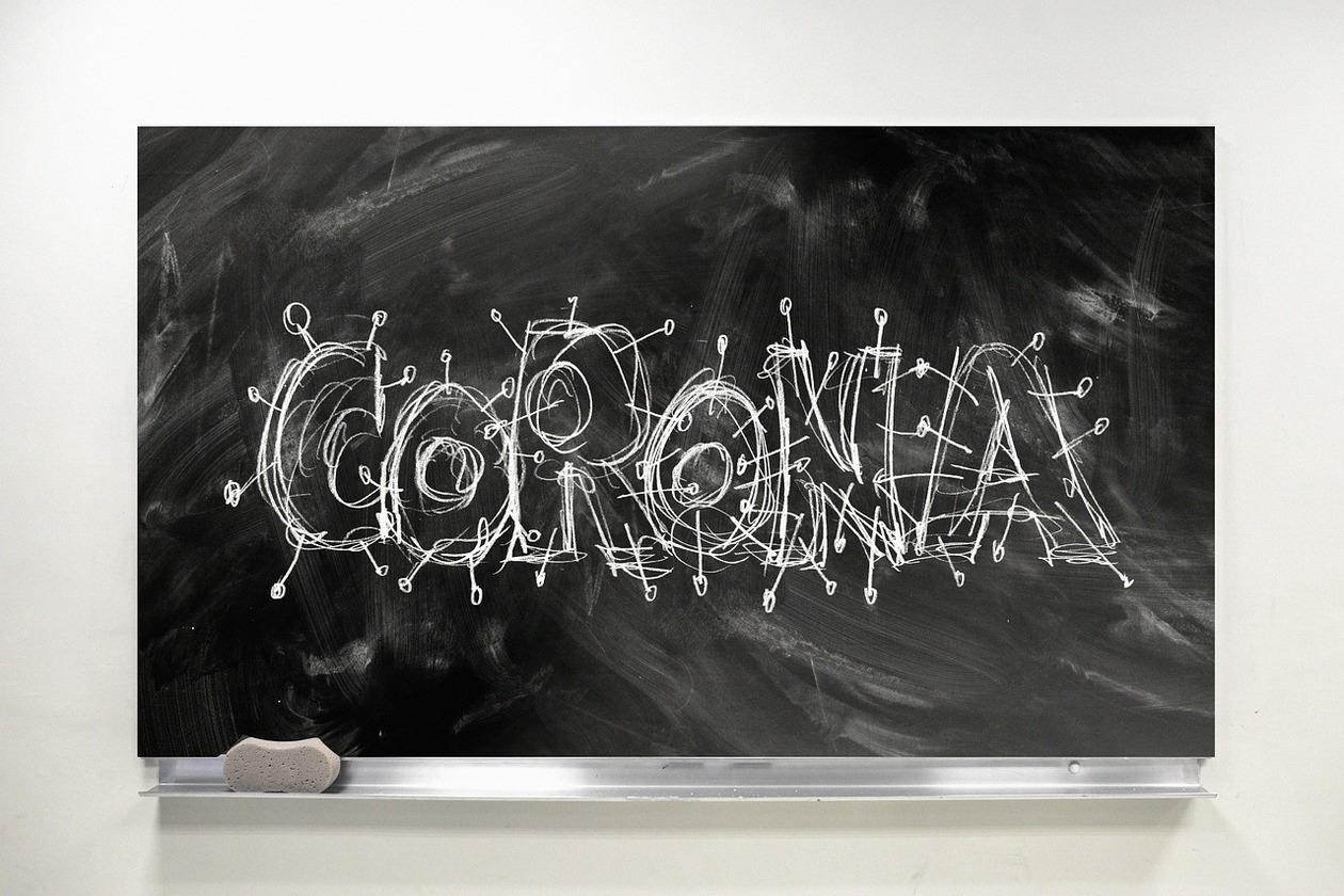 Eine Schultafel, mit Kreide verwischt. Darauf der Kreide-Schriftzug Corona