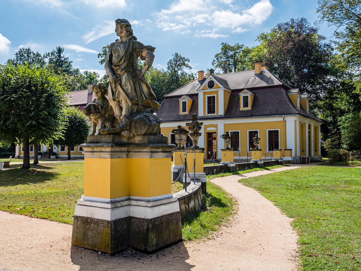 Das Foto zeigt einen barocken Pavillon im Park, davor eine Plastik aus Sandstein.