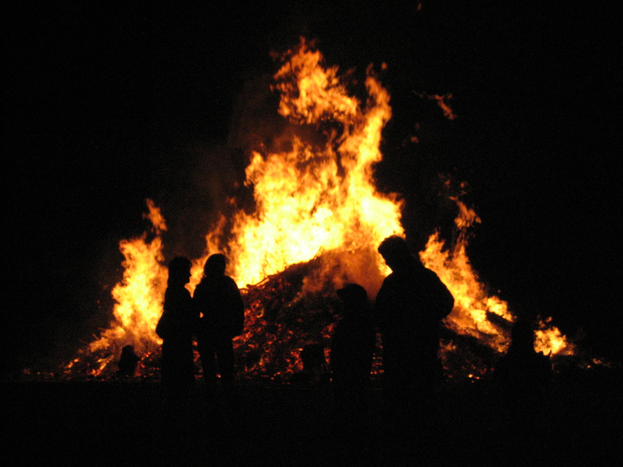 Das Foto zeigt ein großes Feuer in der Nacht, davor schemenhaft Menschen