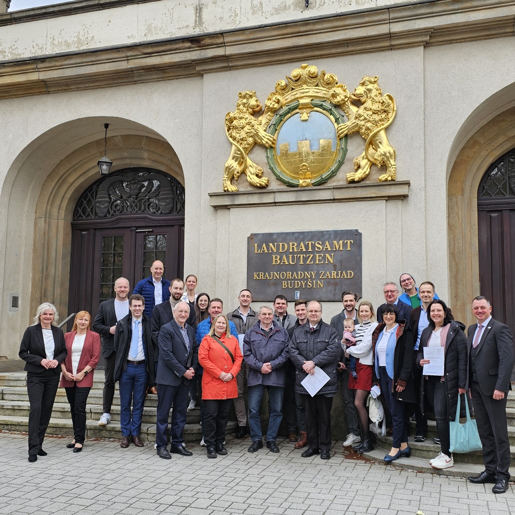 Vor dem Eingangsbereich des Landratsamtes in der Bautzener Bahnhofstraße 9 stehen Frauen und Männer. Einige halten Fördermittelbeschiede in den Händen.