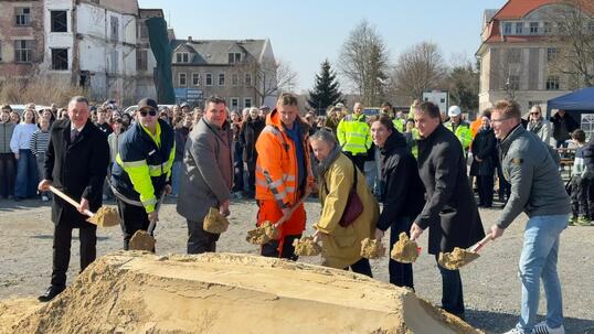 Acht Menschen mit Spaten stehen vor einem Sandhaufen.
