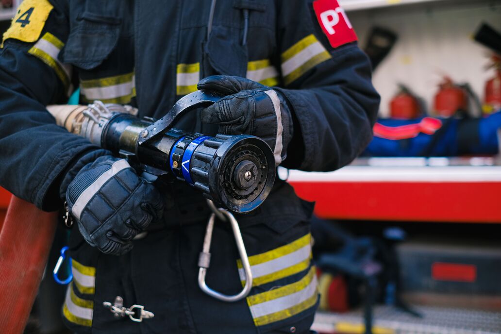 Detailaufnahme: Ein Feuerwehrschlauch in den Händen eines Feuerwehrmannes