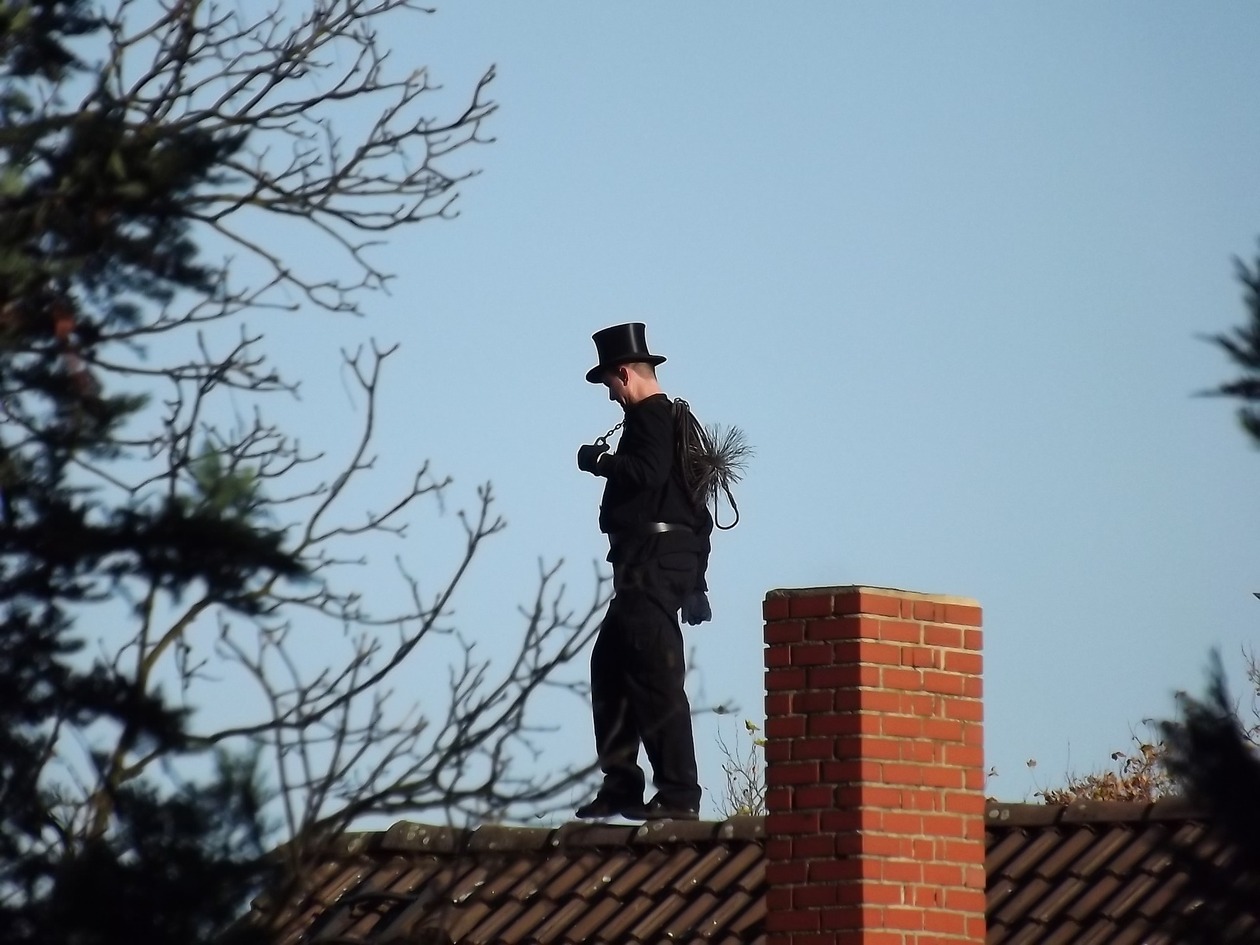 Ein Schornsteinfeger steht auf einem Dach