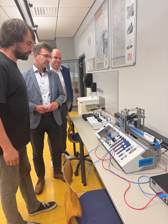 Drei Männer schauen auf ein Bord mit diverser Technik.