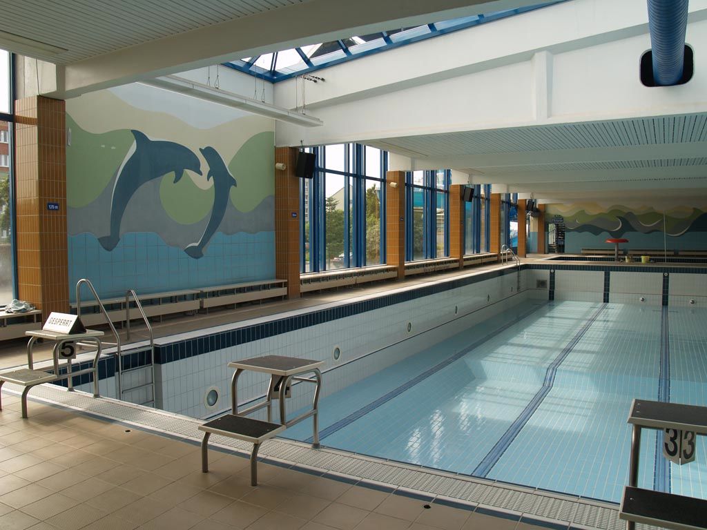Schwimmbecken eines Hallenbades, Fensterfront und Delphin-Mosaik an der Wand