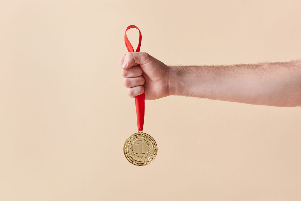 Symbolbild: Ein ausgestreckter Arm, die Hand hält eine Medaille