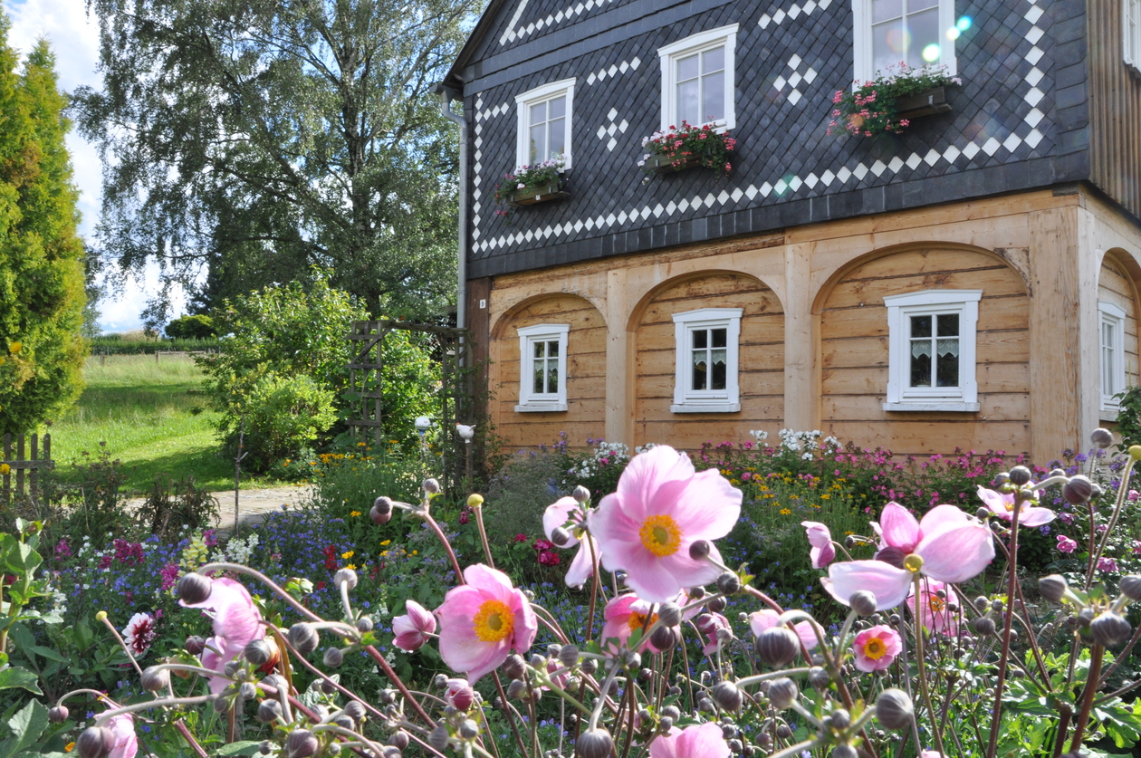 Giebelseite eines Umgebindehauses, davor blühende Blumen im Bauerngarten