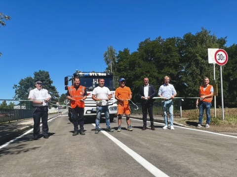 über eine Straße ist ein Band gespannt, hinter dem Band stehen sieben Personen mit einer Schere
