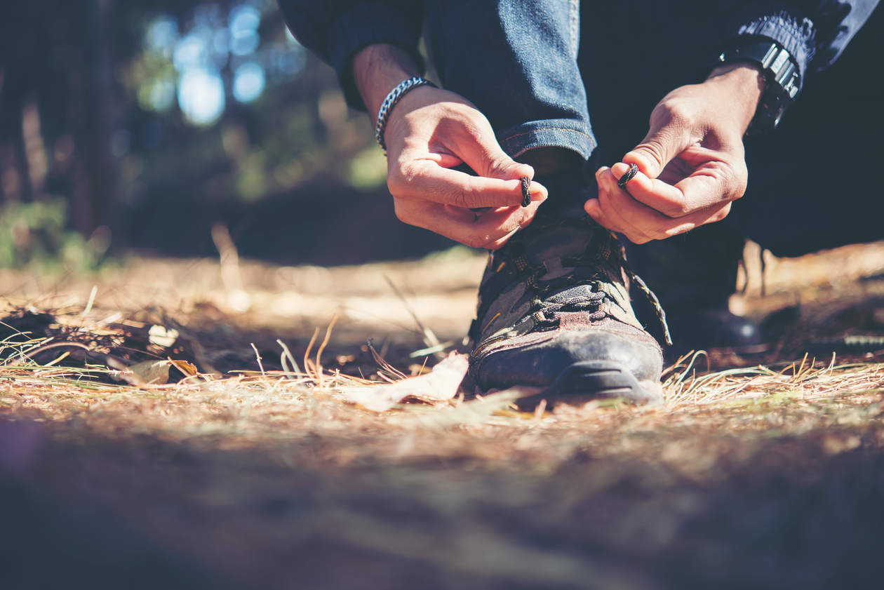 Mann bindet die Schnürsenkel auf seinem Wanderschuh im Wald