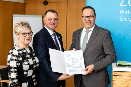 Eine Frau und zwei Männer halten eine Mappe mit Dokumenten in die Kamera