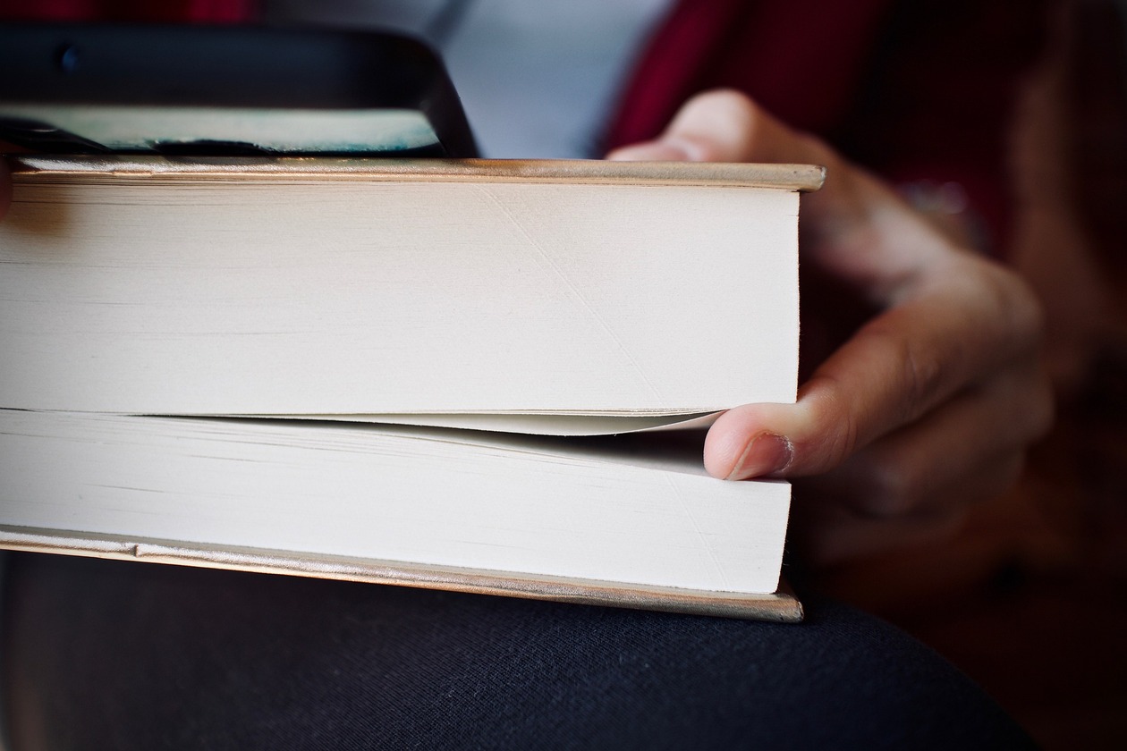 Ein Buch in einer Hand. Ein Finger ist als Lesezeichen zwischen die Seiten geschoben