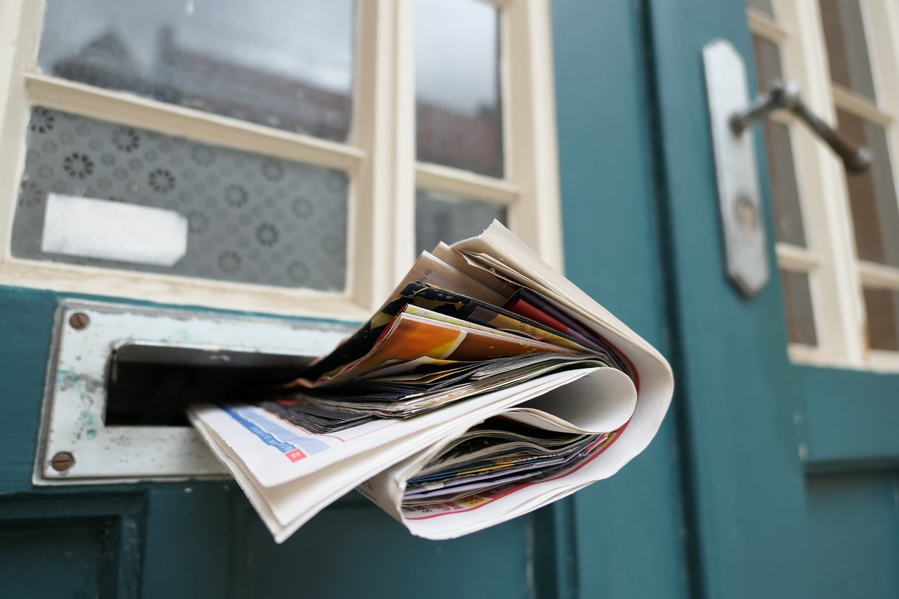 Eine Haustür mit Briefschlitz, darin steckt eine Zeitung.