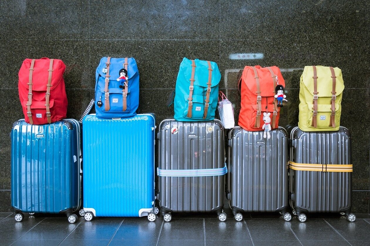 Fünf Rollkoffer stehen vor einer Wand, auf jedem Koffer ein Rucksack